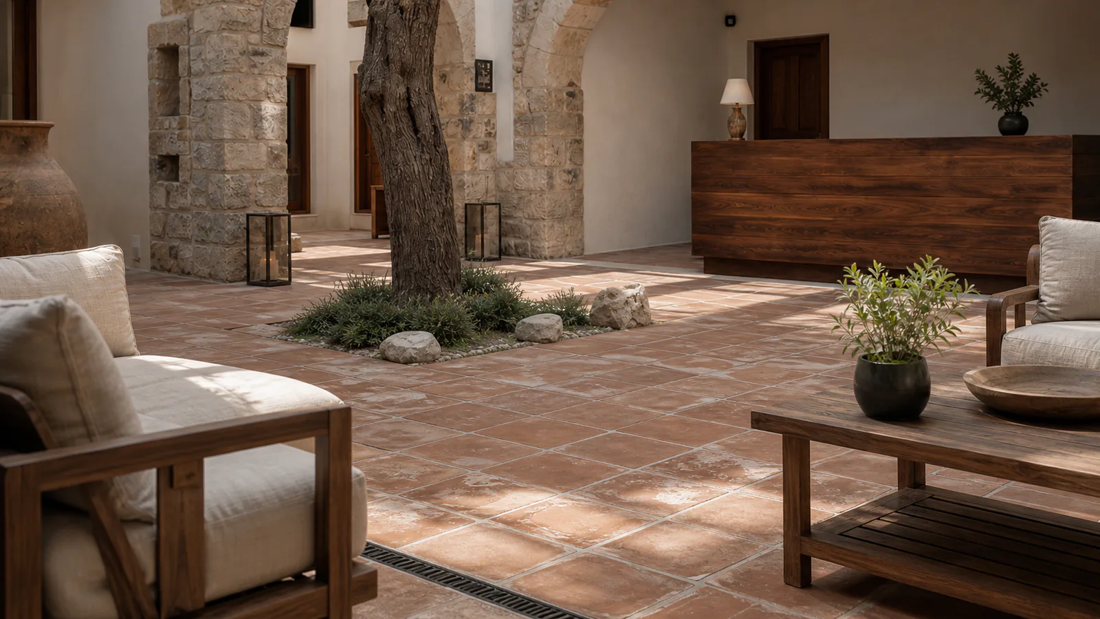 Terracotta döşeme, zeytin ağacı ve keten minderli ceviz oturma gruplarıyla butik otel avlusu